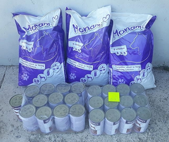 3 sekker med 10 kilo hundemat i hver sekk står lent opp til en hvit murvegg. De er lilla og hvite og det står Monami øverst på sekkene. Foran sekkene er det to brett med hundemat i bokser. Det er tolv i hver pakke og de er pakket inn i plast.